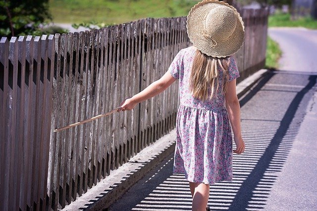 柵に手をかけながら歩く麦わら帽子の女の子
